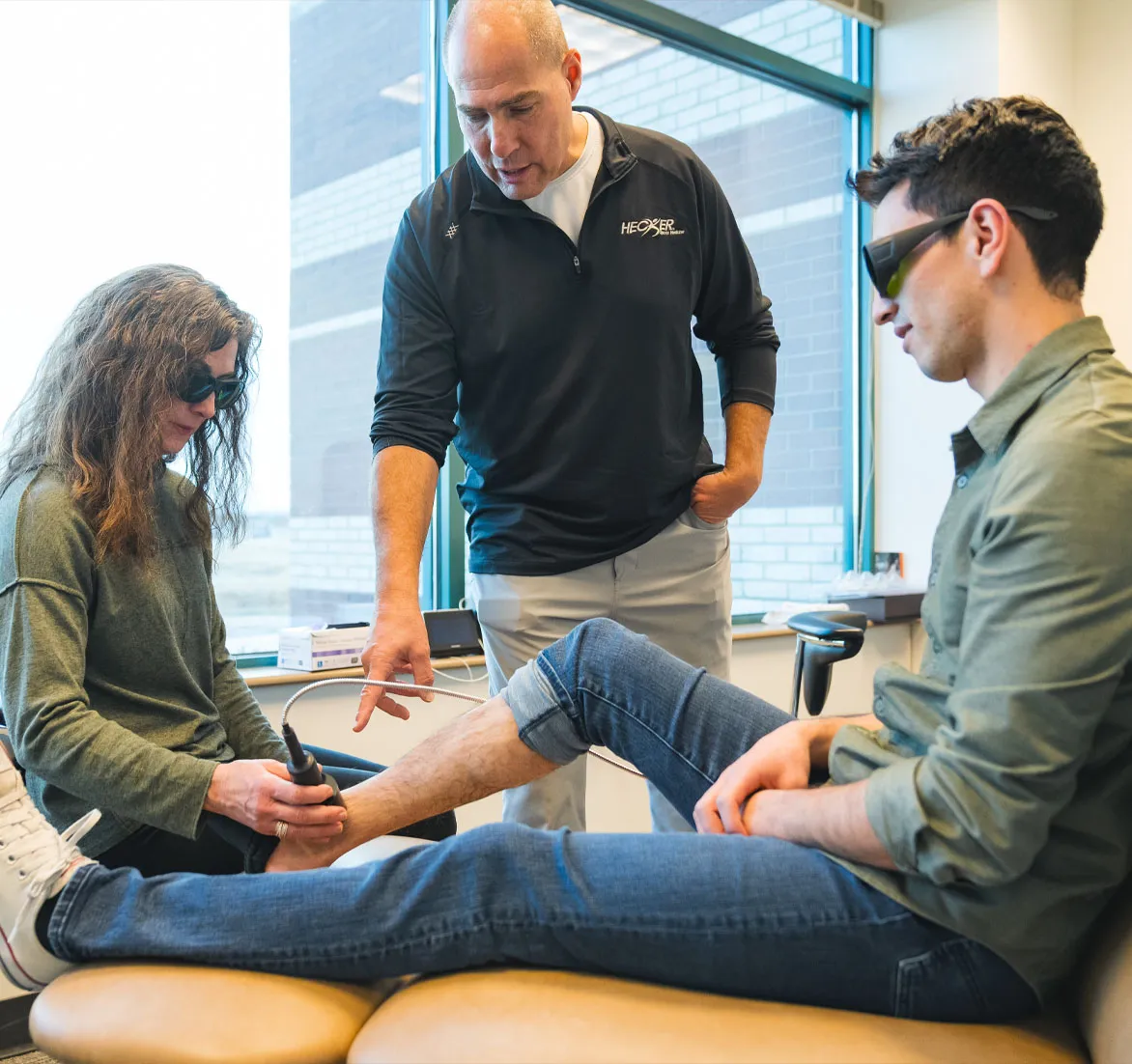 Dr. Hecker treating a patient's ankle while another patient looks on